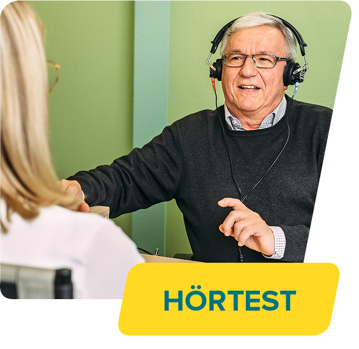 Ein älterer Mann macht einen Hörtest, indem er Kopfhörer trägt und auf Anweisungen der Hörakustikerin reagiert, unten im Bild ein gelbes Banner mit 'HÖRTEST'.