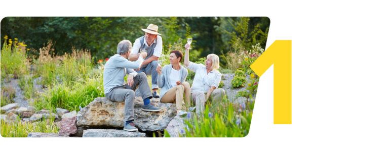 Vier fröhliche Senioren genießen gemeinsam einen entspannten Moment bei einem Glas Wein in einem blühenden Garten, wobei die Zahl 1 in der Ecke des Bildes auffällt.