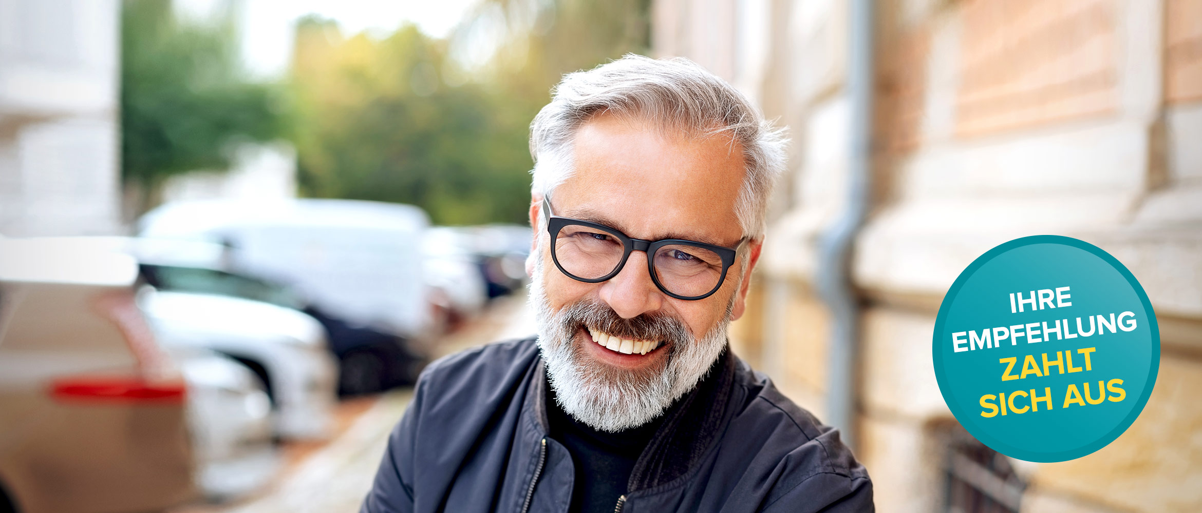 Ein fröhlicher Mann mit grauem Bart und Brille lächelt in die Kamera, auf der rechten Seite steht 'Ihre Empfehlung zahlt sich aus' über einem türkisen Banner.