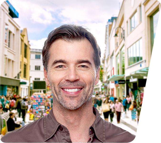 Lächelnder Mann mittleren Alters vor unscharfem Hintergrund einer belebten Einkaufsstraße, symbolisiert Zufriedenheit und Urbanität.