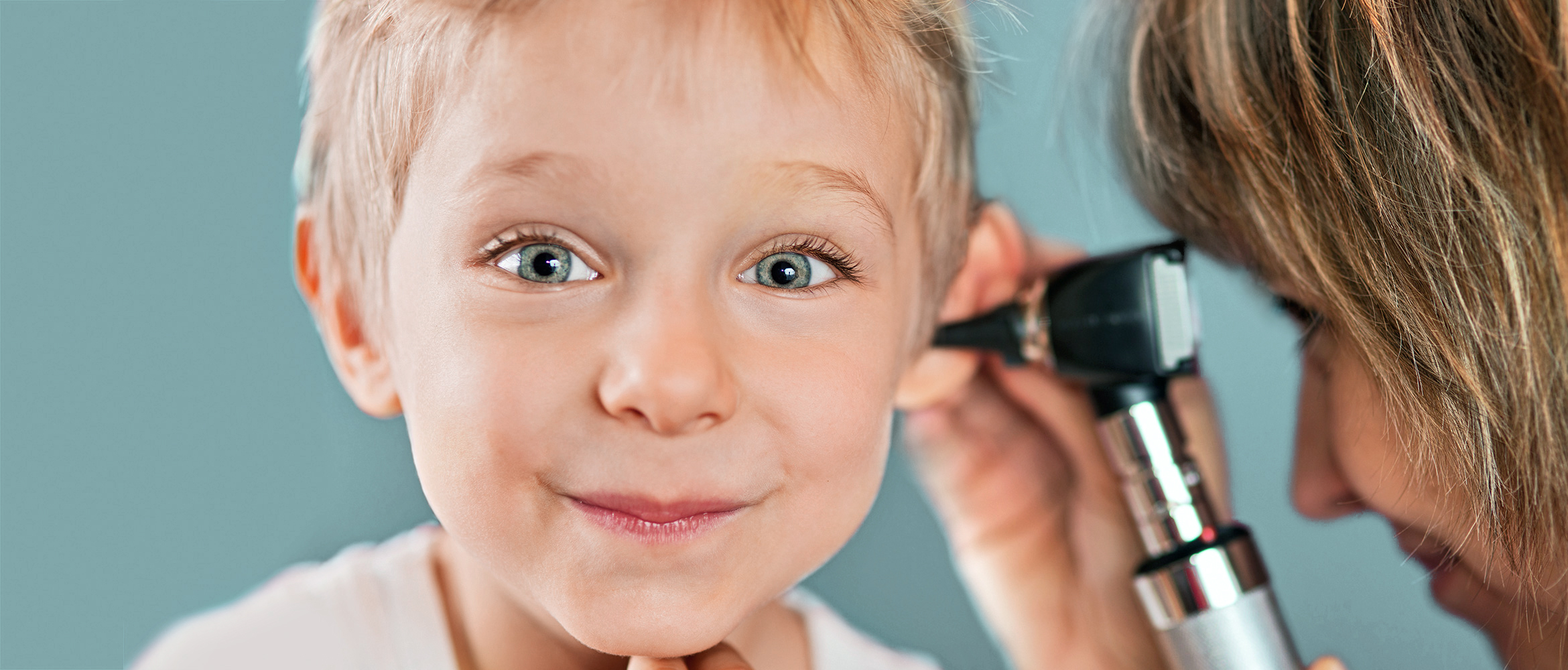 Ein kleiner Junge mit aufmerksamem Blick erhält eine Ohrenuntersuchung durch eine Fachkraft, was die Bedeutung regelmäßiger Hörprüfungen von Kindesbeinen an unterstreicht.